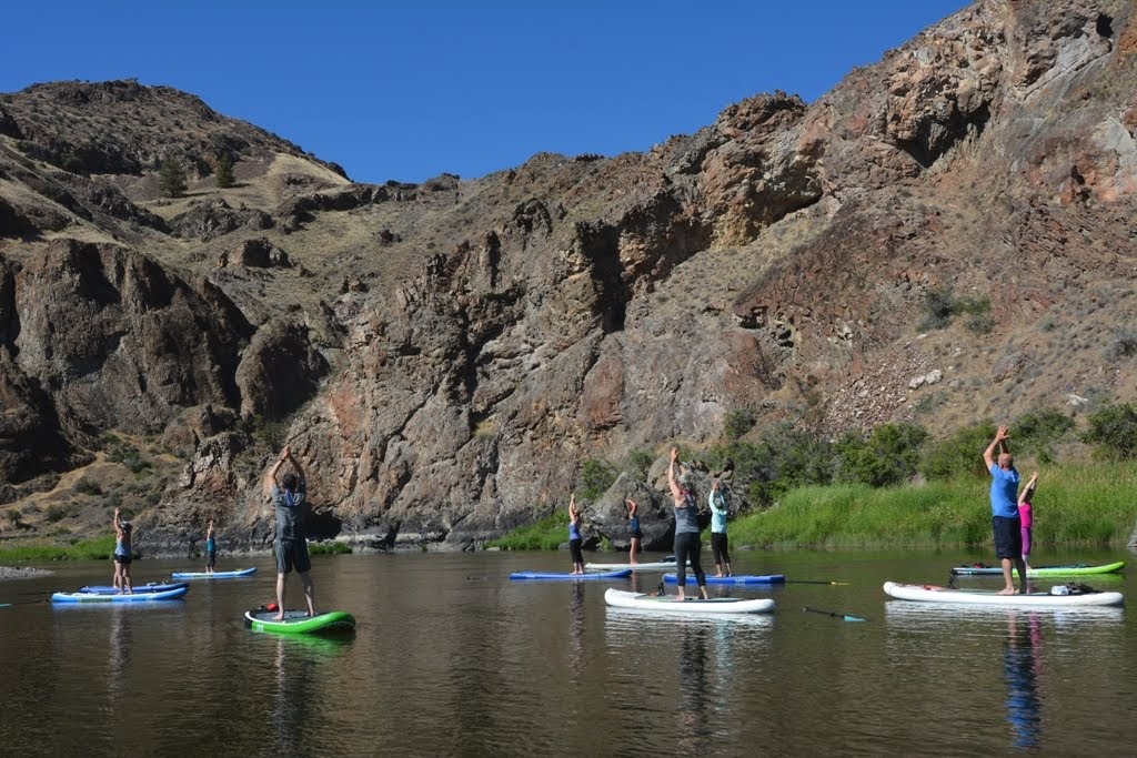 Group of people standing on paddleboards doing yoga on the John Day River