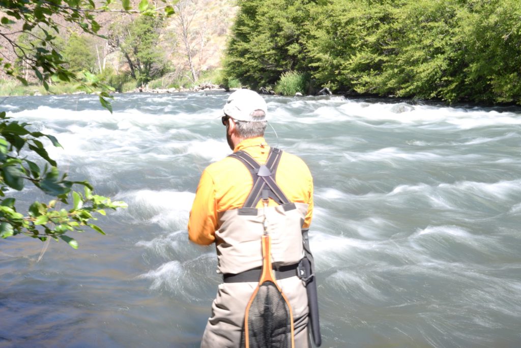 Man in fishing gear standing in front of river with small rapids