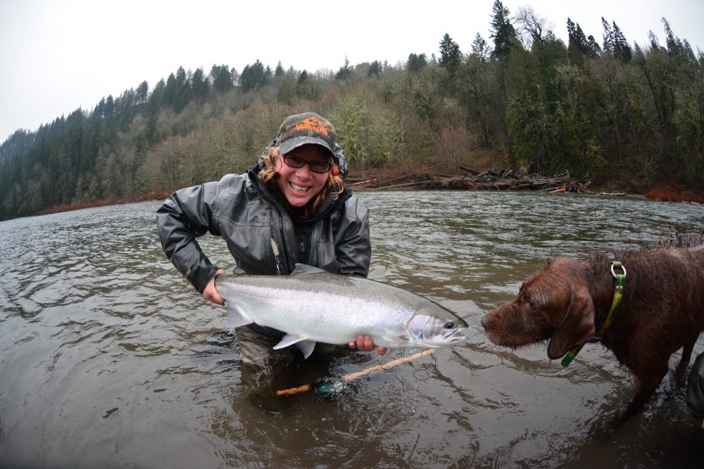 Guide, Mia, and dog standing in the Sandy River holding a steelhead she caught