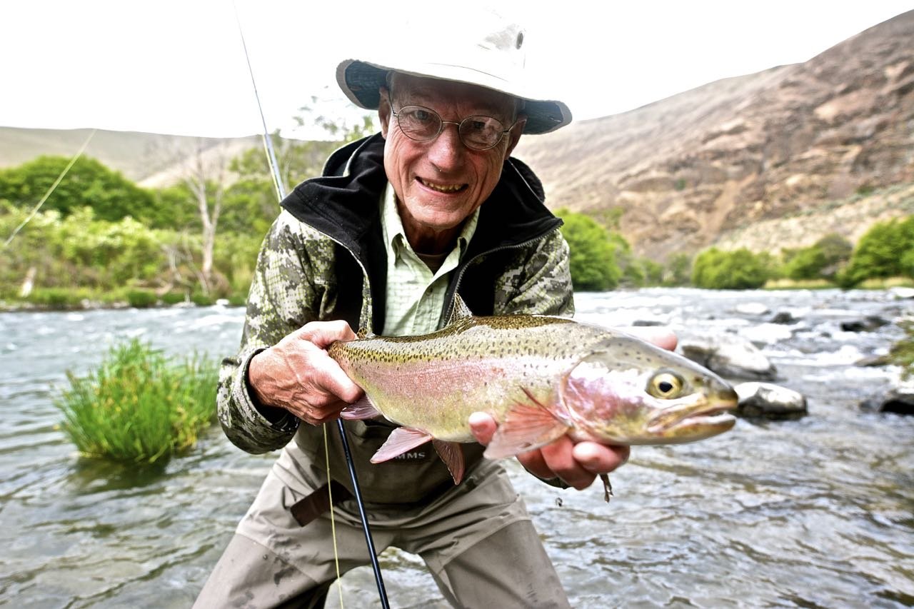 Man smiling standing in front of the Deschutes River holding a trout he caught
